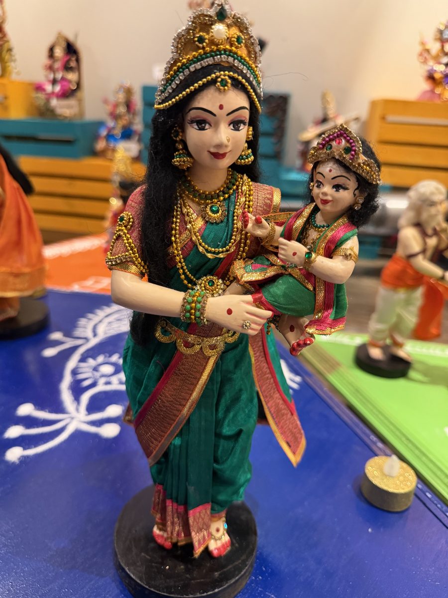 Golu doll of a Karthigai maiden in a green sari carrying baby Murugan on her hip