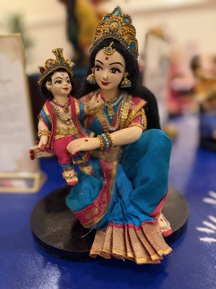 Golu doll of a Karthigai maiden in a teal sari, seated, playing with baby Murugan