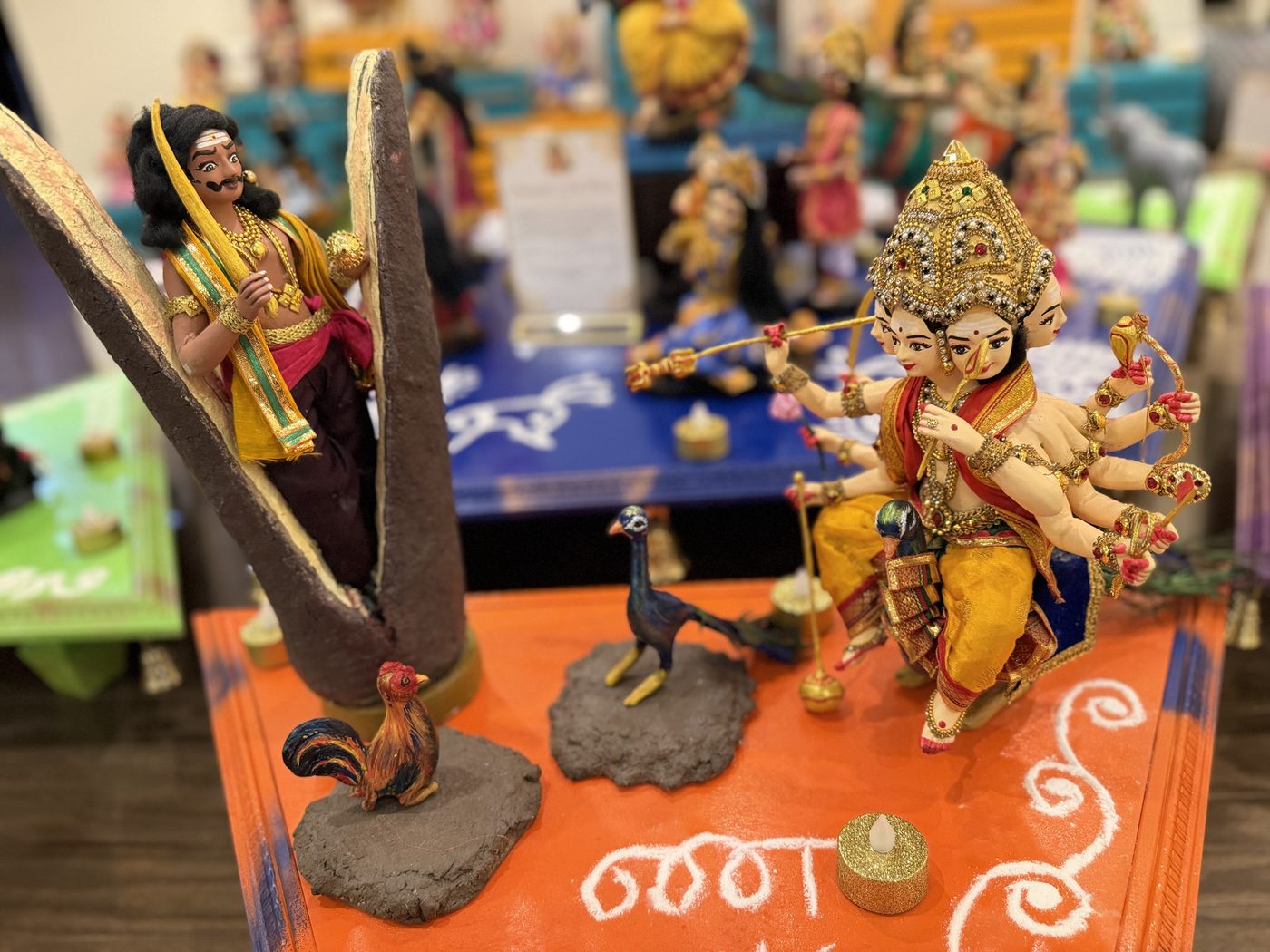 Golu dolls of Surapadman inside a split mango tree facing Shanmukha on his peacock, with a rooster and a peacock between them