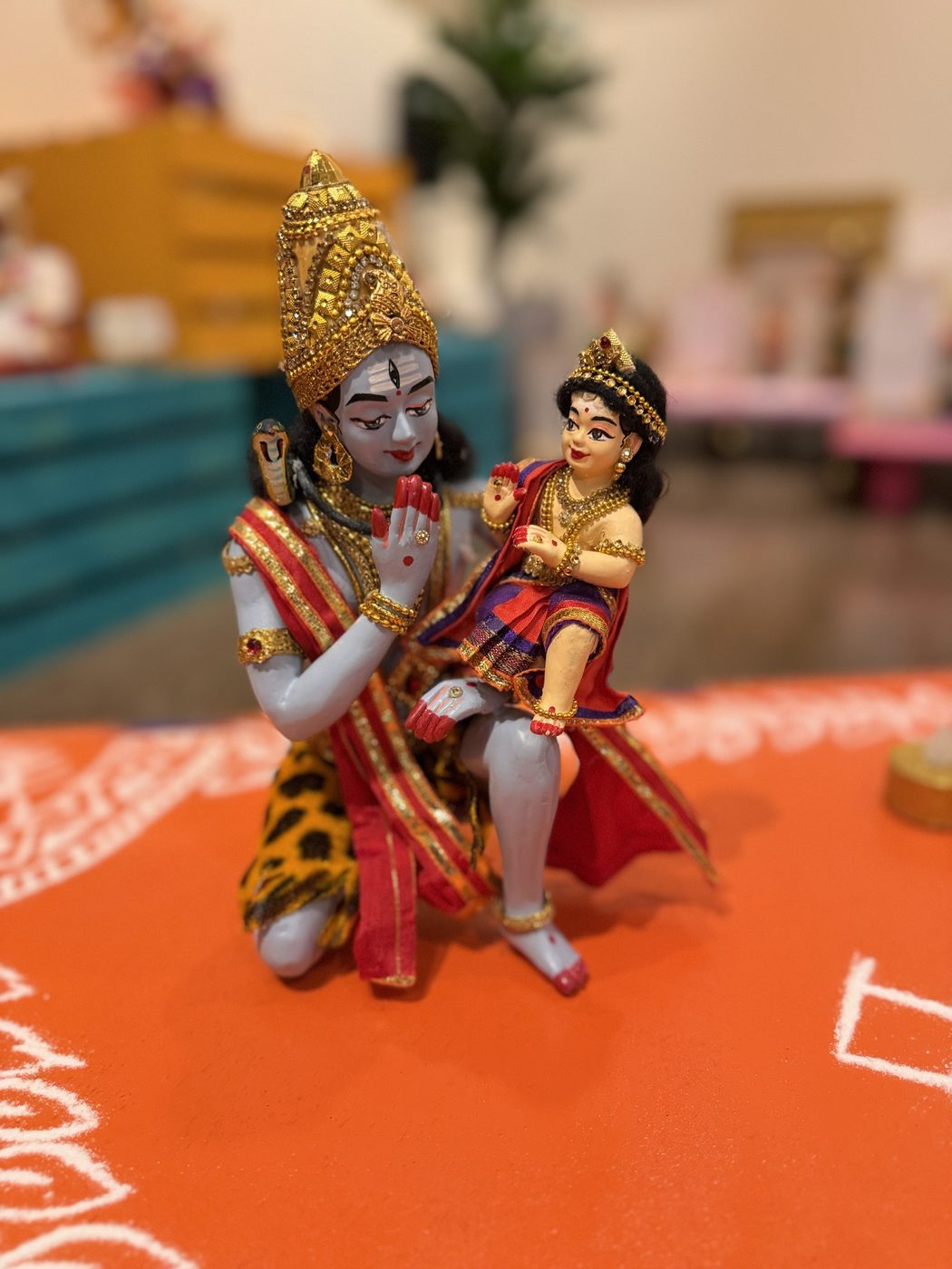 Golu doll of Shiva kneeling with his hand raised in respect while little Murugan sits on his knee